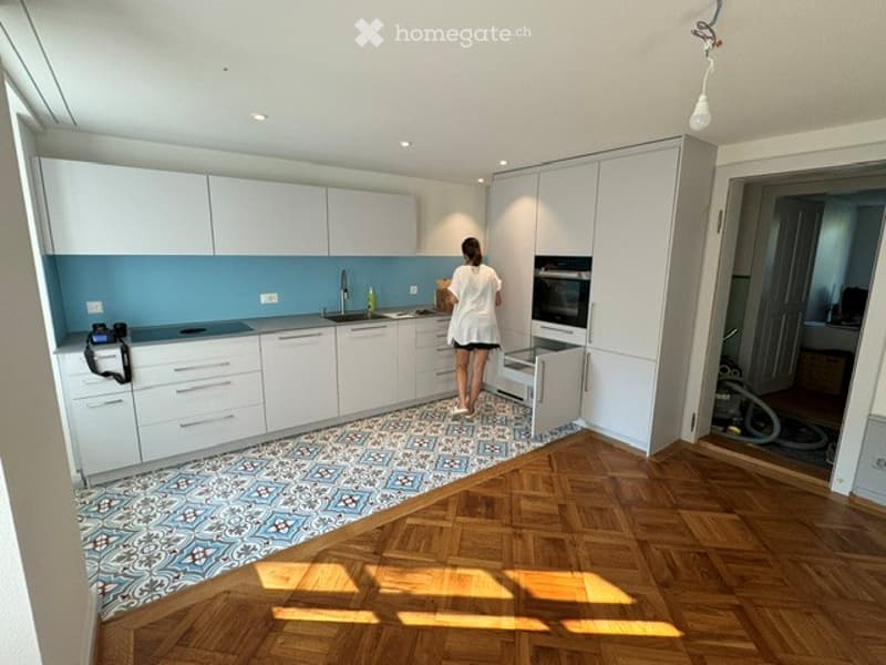 Modern kitchen with white cabinets, blue backsplash, wooden floor, and stainless steel appliances. A person is seen cleaning the area.