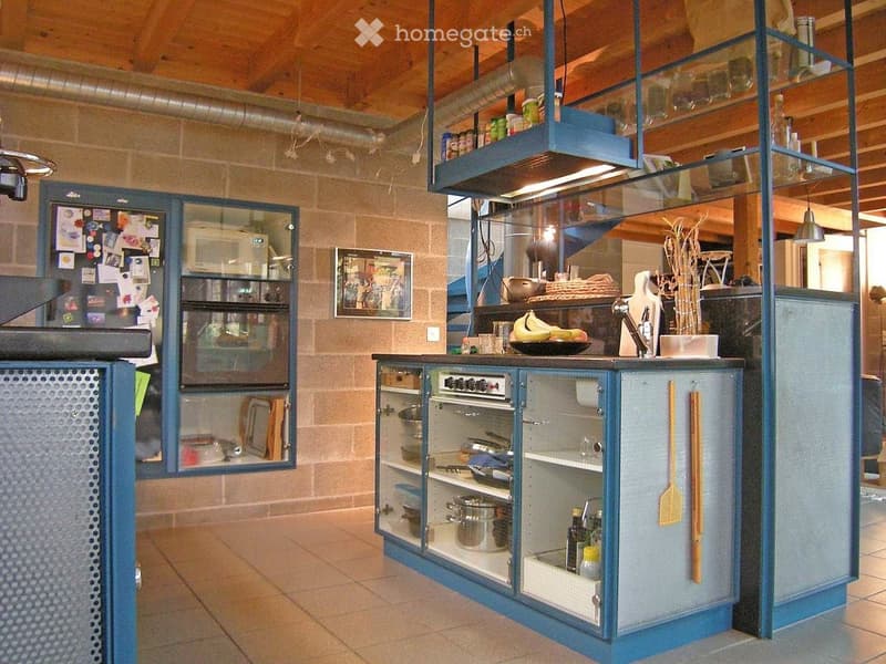 Modern kitchen with blue cabinets, stainless steel appliances, and a central island. Features include a refrigerator, oven, and various kitchen utensils and items on the counter and shelves.