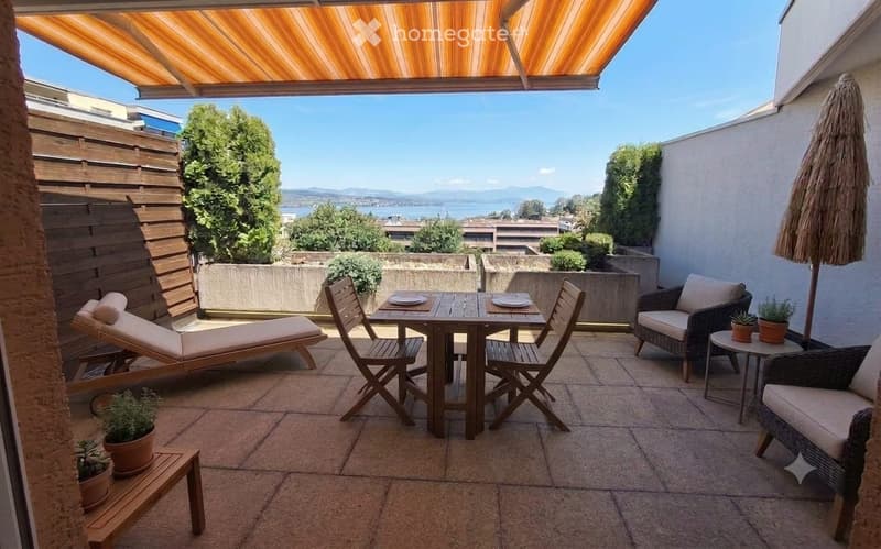 Balcony with a view, featuring a wooden table, chairs, lounge chair, umbrella, and potted plants.