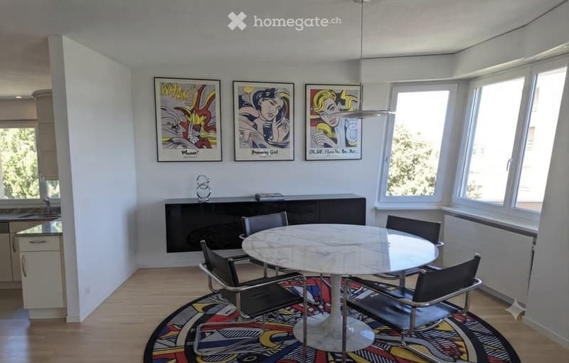 Modern dining area with a round marble table, four black chairs, a sleek black cabinet, and colorful abstract artwork on the walls. Large windows allow natural light to fill the space.