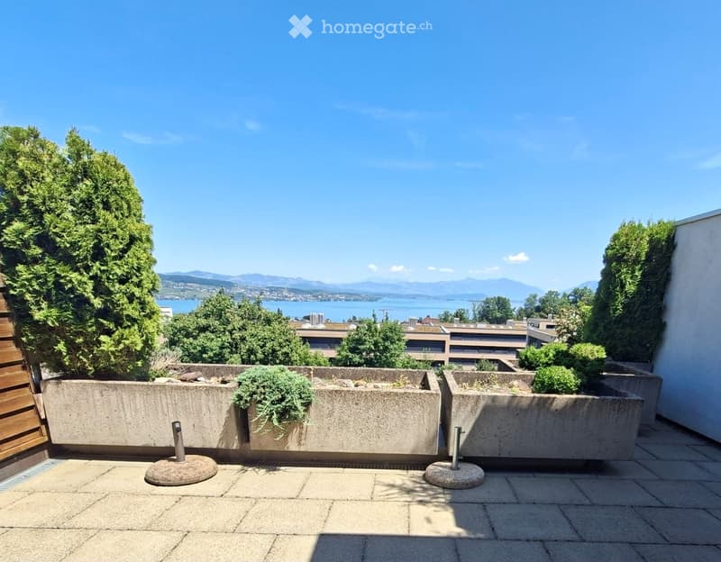 Balcony with concrete planters, tiled floor, and scenic view of a lake and mountains.