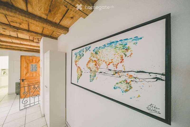 A room with a colorful abstract painting of a world map on the wall, wooden ceiling beams, and a tiled floor.