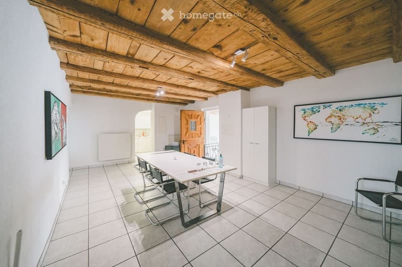 Bright room with exposed wooden ceiling beams, tiled floor, and modern furniture including a table, chairs, and a large world map on the wall.