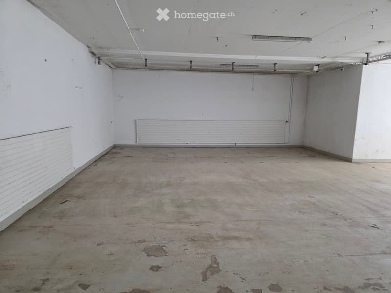 Empty room with white walls, concrete floor, and exposed ceiling pipes and lighting fixtures.