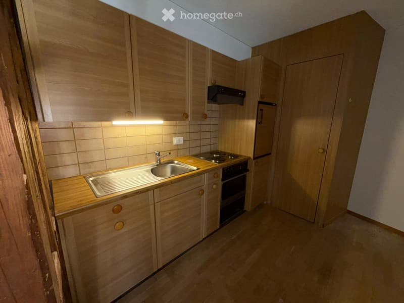 Compact kitchen with wooden cabinets, a sink, stove, and oven. The space features tiled walls and a wooden countertop.