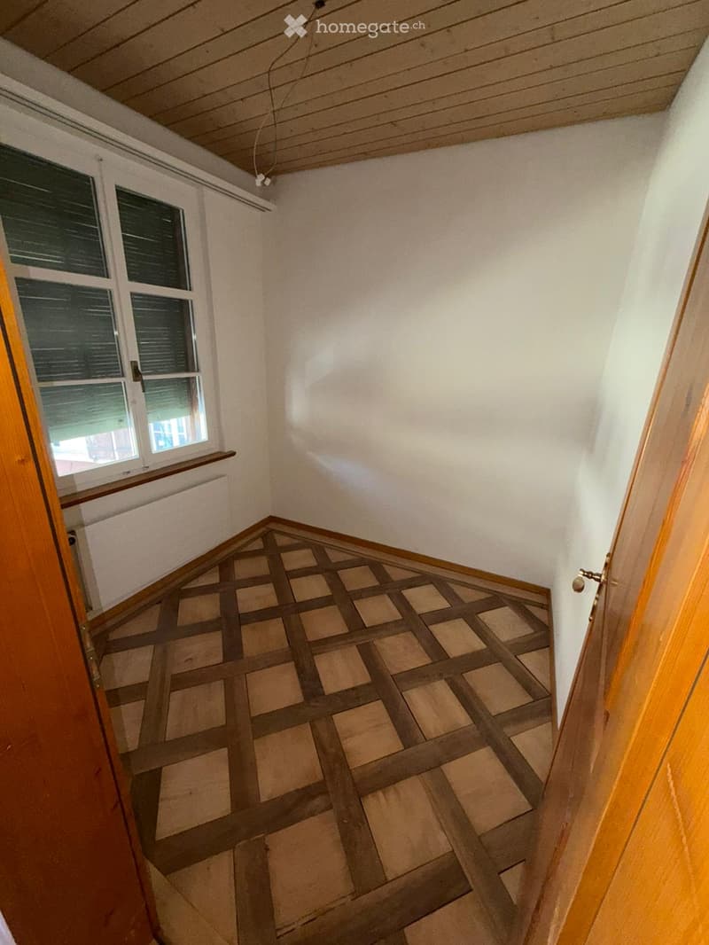 Empty room with wooden floor and white walls, featuring a window with blinds and a radiator below it.