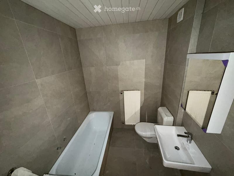 Bathroom with a bathtub, toilet, sink, and radiator. Beige tiled walls and floor.