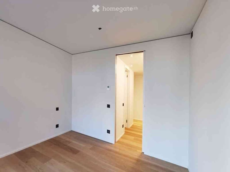 Empty room with light-colored wooden flooring and white walls, featuring an open doorway leading to another room.