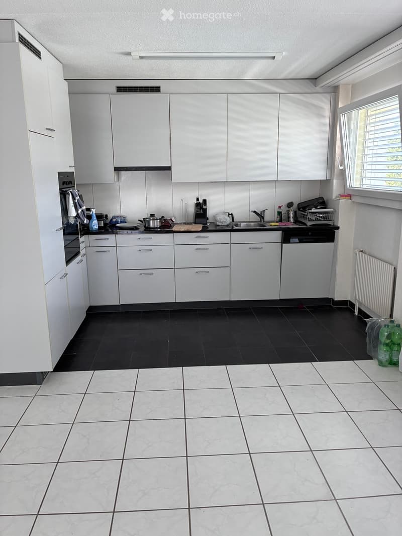 Modern kitchen with white cabinets, black countertops, and stainless steel appliances. Includes a sink, oven, dishwasher, coffee maker, and various kitchen items on the counter.