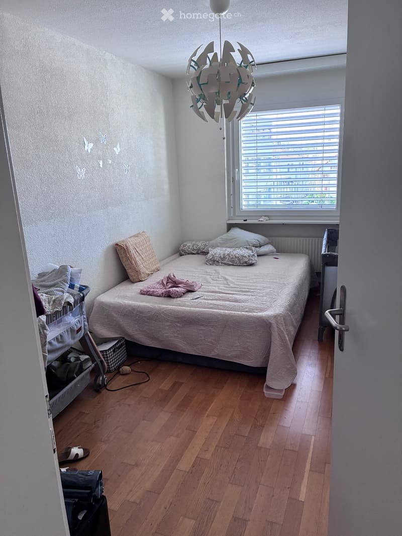 Cozy bedroom with wooden flooring, a single bed with pillows and a blanket, a radiator, a storage unit, and a decorative lamp hanging from the ceiling.