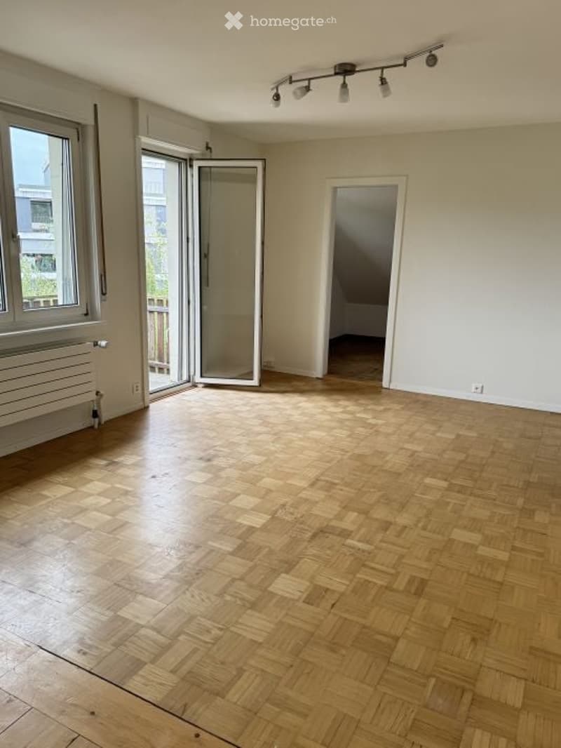 Empty room with wooden parquet flooring, large windows, sliding glass door leading to a balcony, and recessed track lighting.