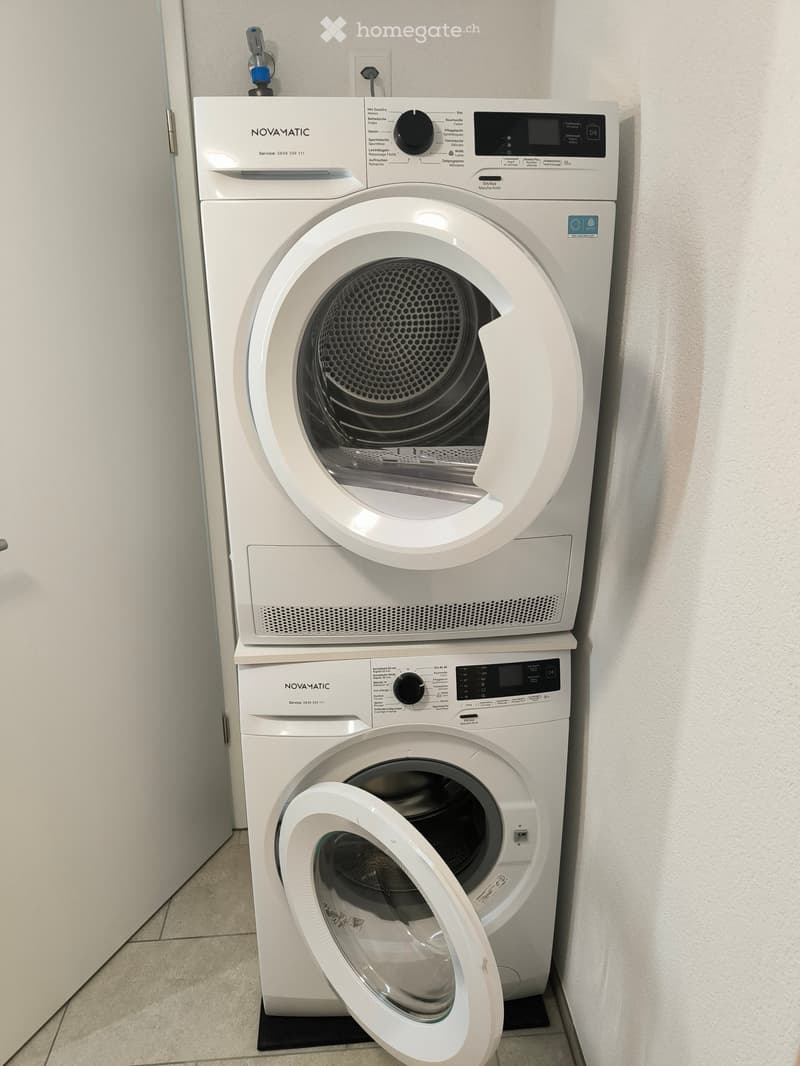 A modern, white washing machine and dryer unit with control panels and digital displays, placed in a tiled room.