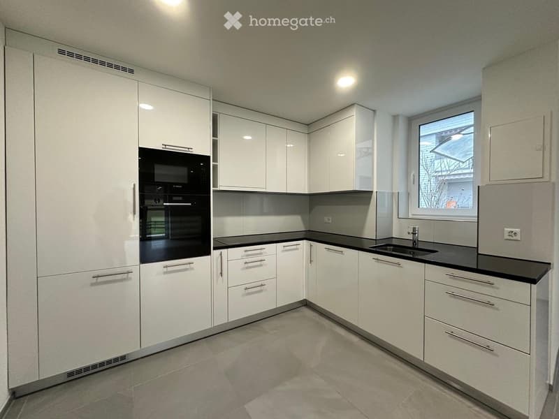 Modern kitchen with white cabinets, black countertops, and built-in appliances including an oven and microwave.