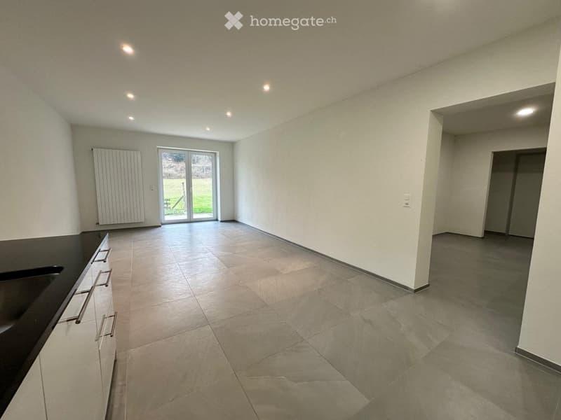 Empty room with tiled floor, white walls, and a large sliding glass door leading to an outdoor area. There is a black countertop with cabinets on the left side.