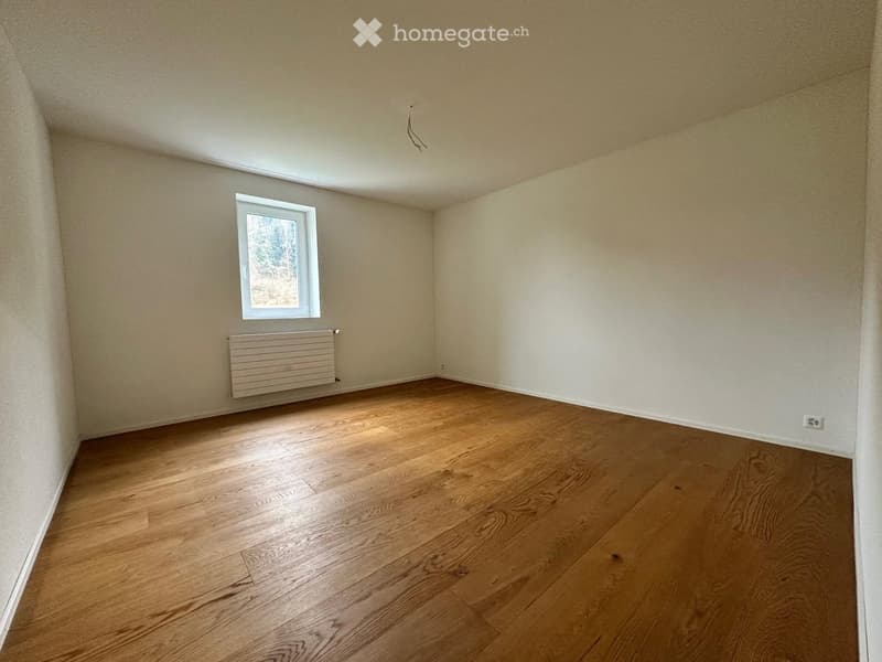 Empty room with wooden flooring, white walls, a single window, and a radiator below it.