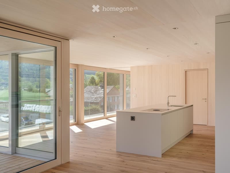 Modern, minimalist kitchen with light wood cabinetry, a central island, and large glass doors opening to a scenic outdoor view.