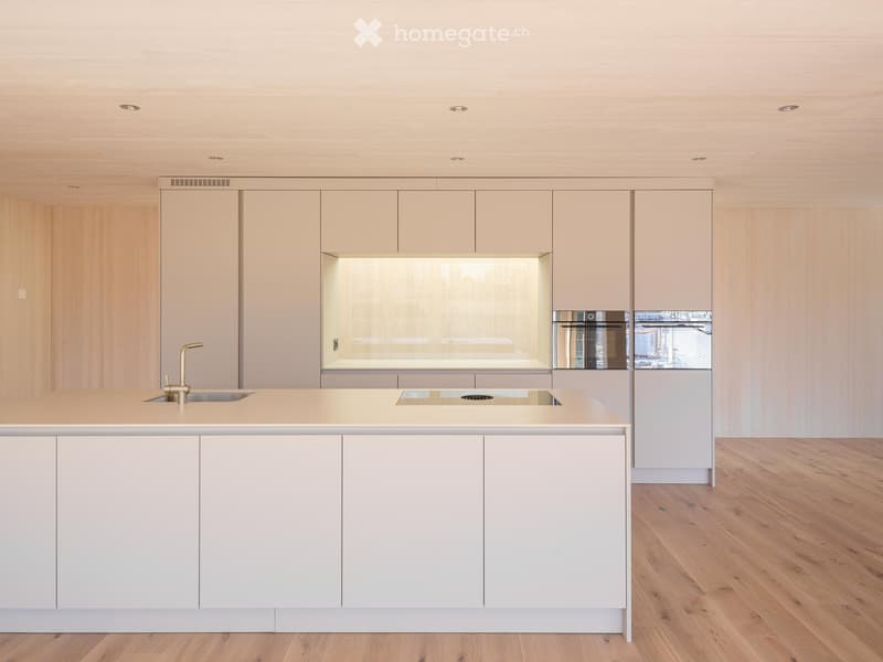Modern kitchen with light-colored cabinets, a central island, and a stainless steel oven. The island features a sink and faucet, and the floor is made of light wood.