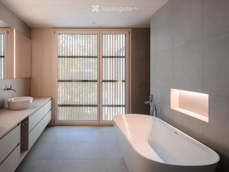Modern bathroom with a freestanding bathtub, sink, and sleek wooden cabinetry. Large glass doors with vertical blinds provide natural light.