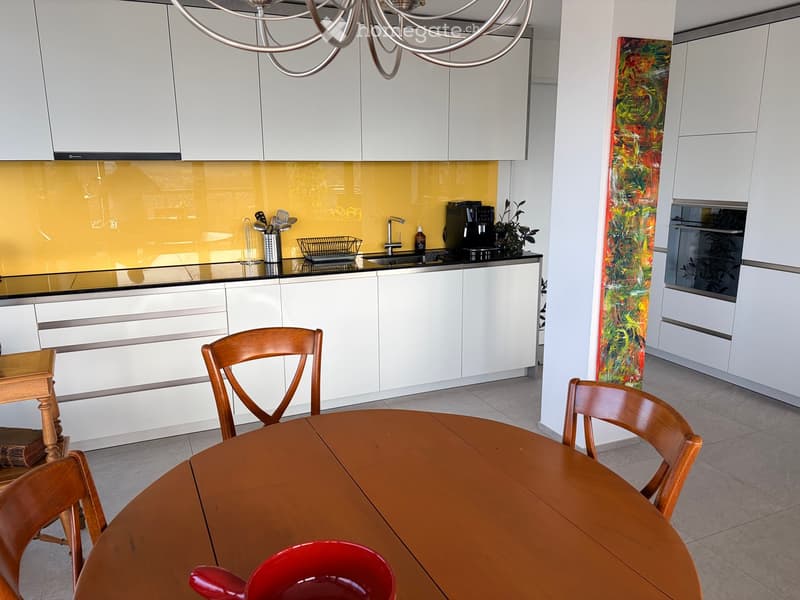 Modern kitchen with white cabinets, a wooden dining table, and a colorful abstract painting on the wall.