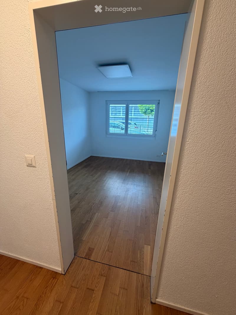 Empty room with wooden flooring, light blue walls, and a window with blinds. No furniture or equipment is present.