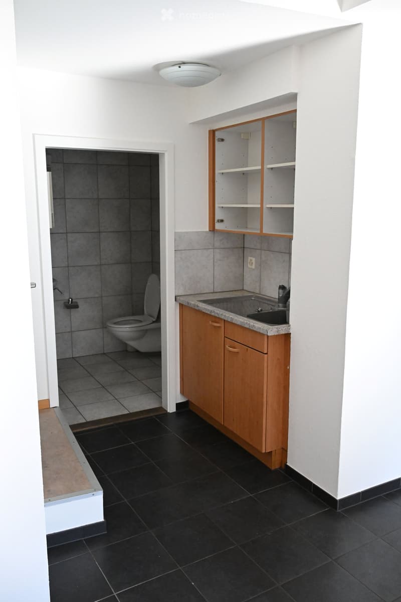 Modern bathroom with black tiled floor, white walls, wooden cabinet, sink, and toilet. Open shelving unit with wooden frame and white shelves.