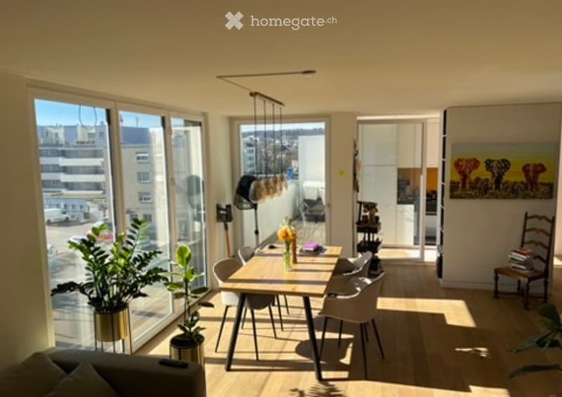 Bright, modern living and dining area with large windows, a sofa, dining table with chairs, potted plants, a floor lamp, and a painting on the wall.