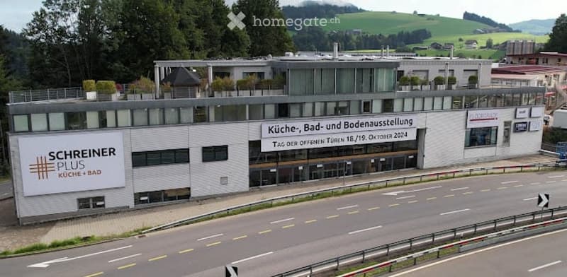 Modern commercial building with signage for "Schreiner Plus Küche/Bad" and "Küche, Bad- und Bodenausstellung. Täg den offenen Türen 15./16. Oktober 2024".