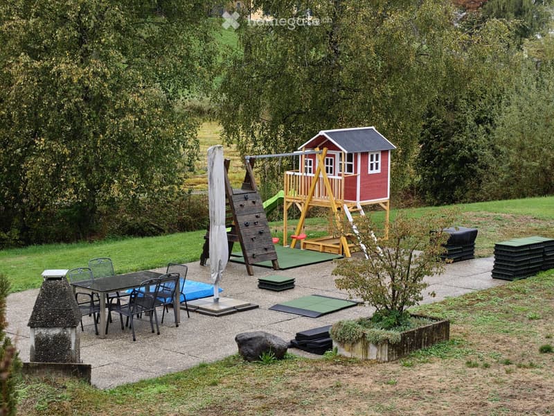 Outdoor play area with a small red playhouse, climbing structure, swing, and a dining set with chairs and table.
