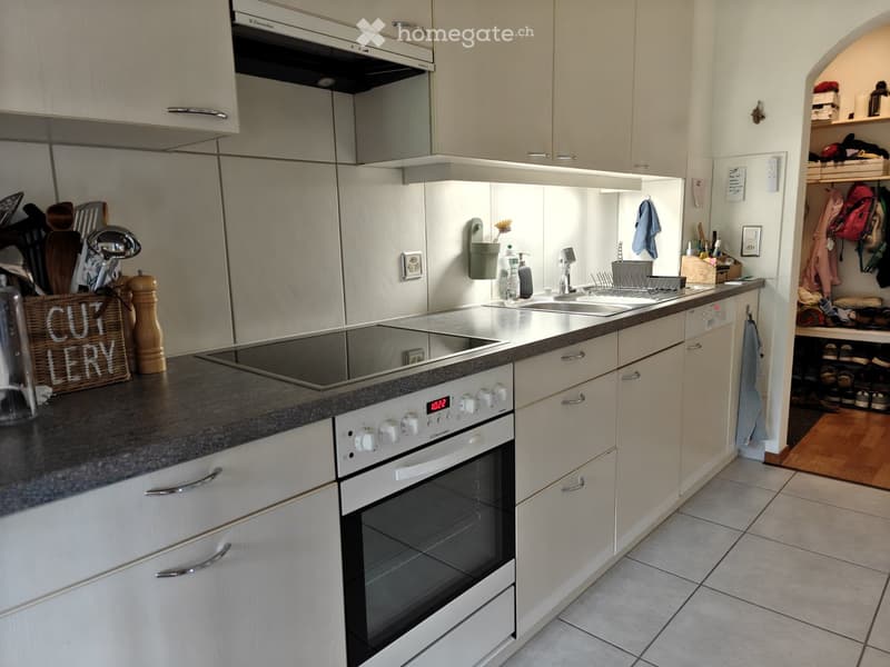 Modern kitchen with white cabinets, stainless steel appliances, and a grey countertop. Features an oven, sink, and various kitchen utensils.