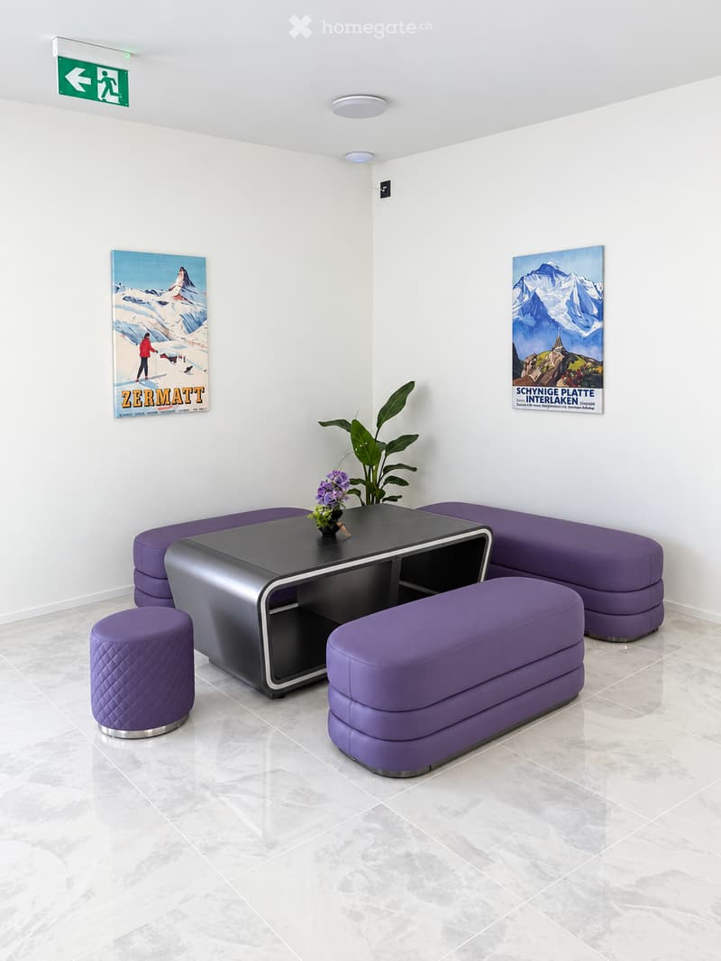 Modern lounge area with white walls, marble flooring, purple seating, and a black table with a flower vase.