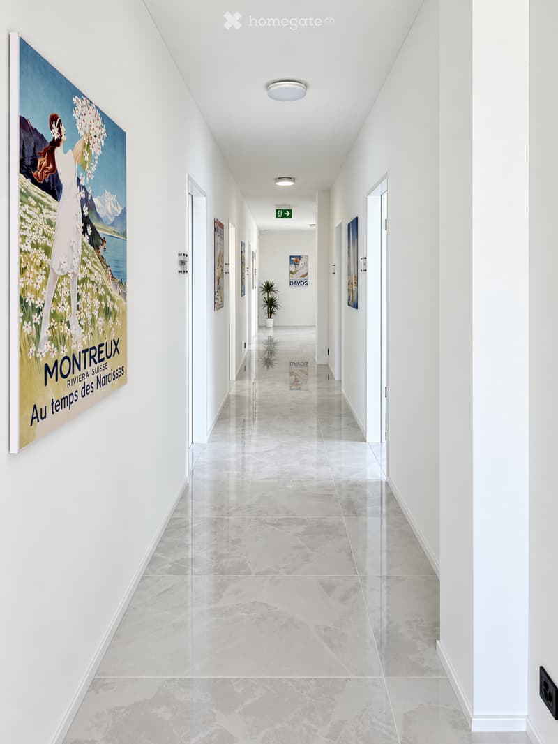 Modern hallway with white walls, polished marble floor, recessed lighting, and framed artwork, including a large poster titled "Montreux."