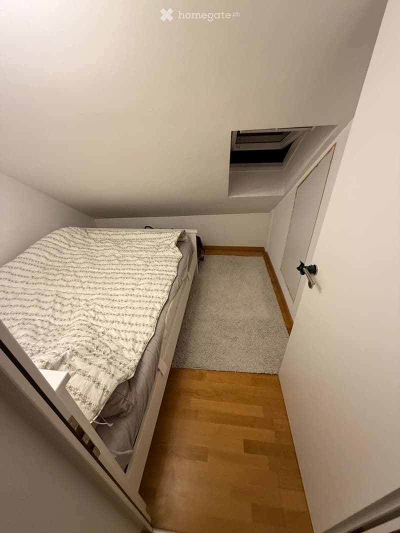 Cozy bedroom with a single bed, light-colored bedding, a small white rug, and wooden flooring.
