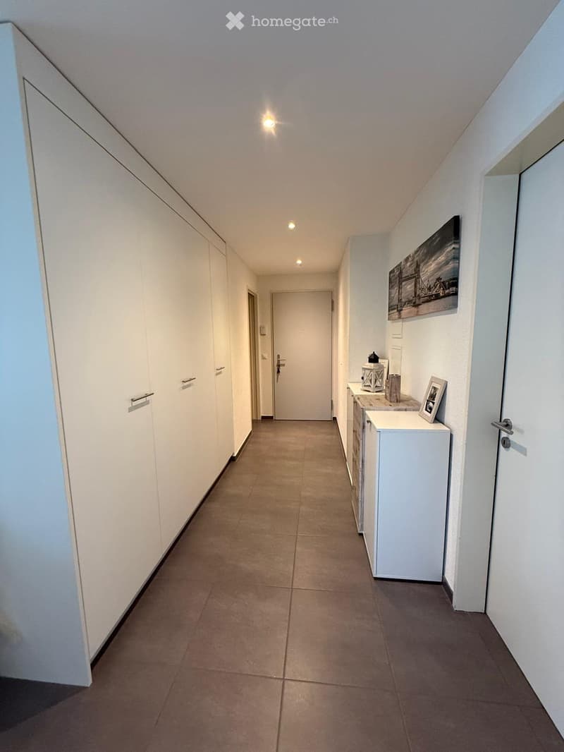 Clean, modern hallway with tiled flooring, white walls, built-in storage units, and a small console table with decorative items.