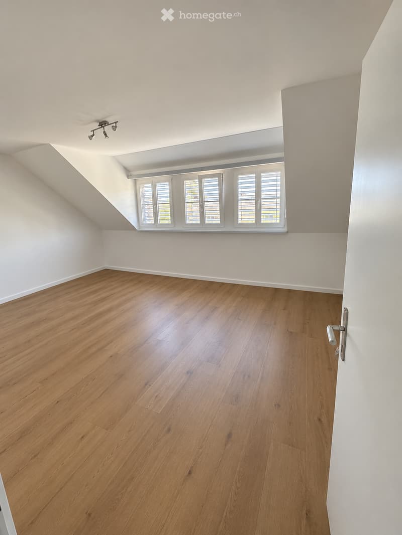 Empty room with wooden flooring, white walls, and large windows with shutters. The ceiling has recessed lighting.