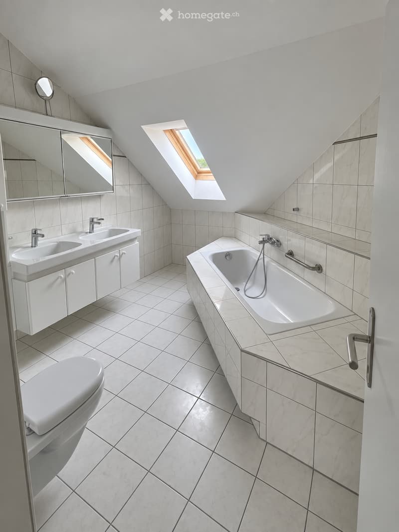 Modern bathroom with white tiles, a large window, a bathtub, a sink, and a toilet.