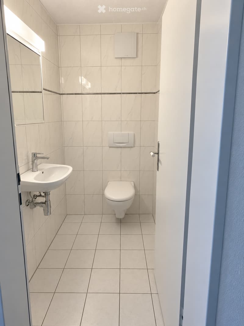 Modern bathroom with white tiles, a sink, toilet, mirror, and light fixture.