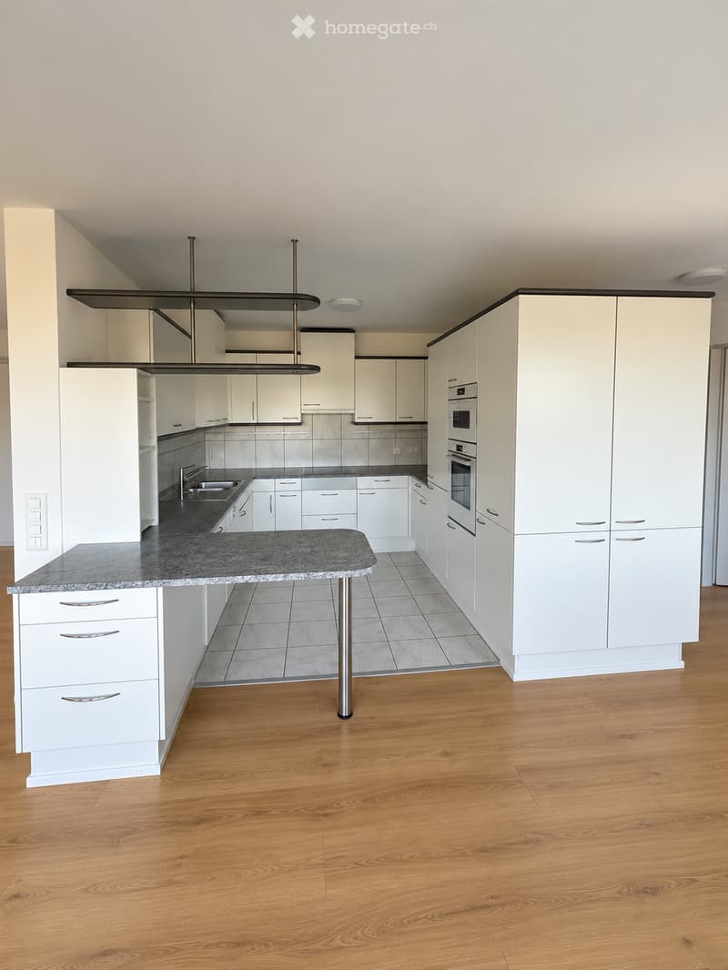 Modern kitchen with white cabinets, granite countertop, island, sink, and built-in oven. Wooden flooring throughout.