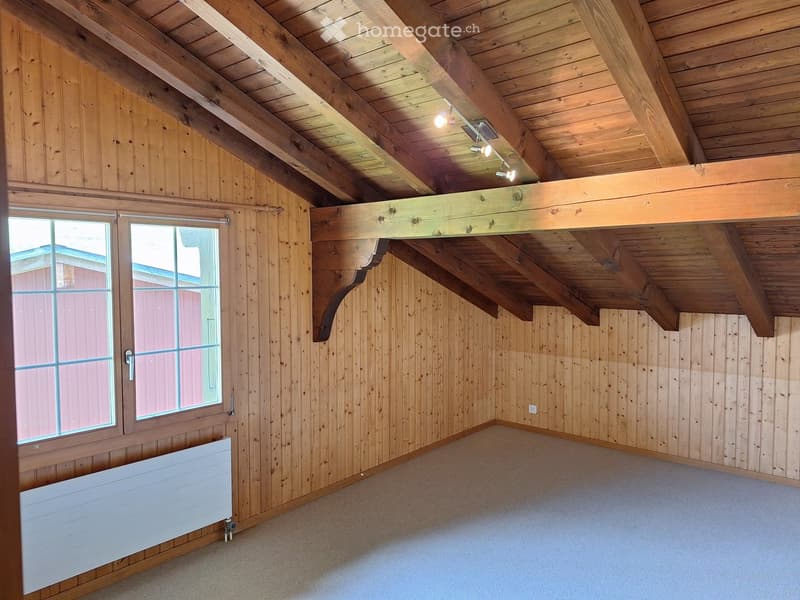 Empty room with wooden walls and ceiling, large windows, exposed wooden beams, and a radiator.
