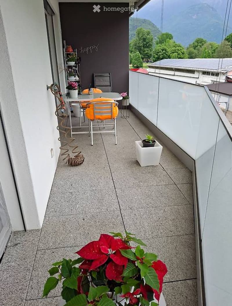 Balcony with a view of mountains, featuring a small table, chairs, and potted plants.