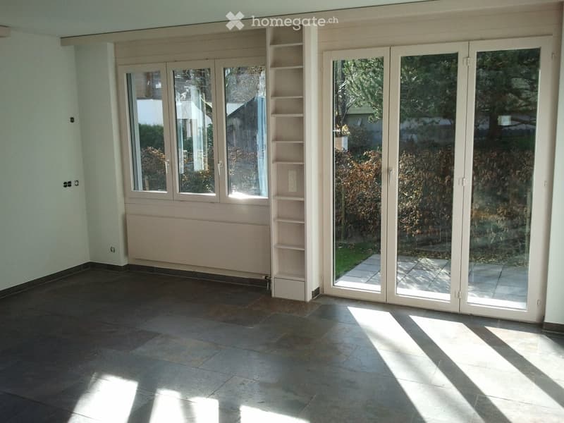 Empty room with tiled floor, large sliding glass doors leading to a patio, built-in shelving unit, and radiator.
