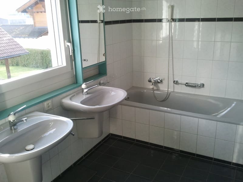 Bathroom with two sinks, a bathtub, and a large window offering a view of the outside. The room features tiled walls and a dark tiled floor.