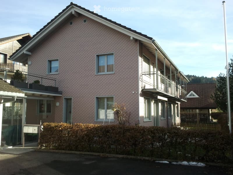 Two-story house with pink siding, multiple windows, balconies, and a small garden area.