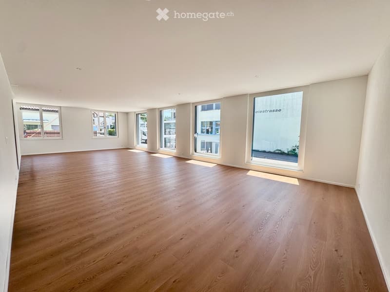Empty room with wooden flooring and large windows, featuring white walls and a clean, minimalist design.