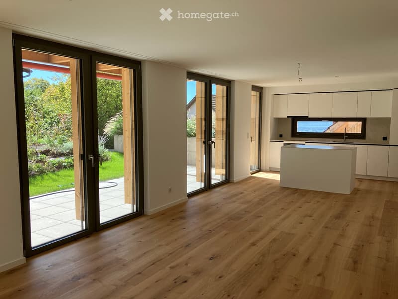 Bright, open-plan space with light wooden flooring, large sliding glass doors leading to a garden, and a modern kitchen area with white cabinets and a central island.