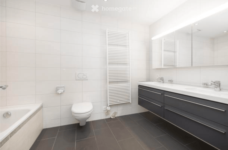 Modern bathroom with white tiles, black tiled floor, bathtub, toilet, sink with mirror, and radiator.