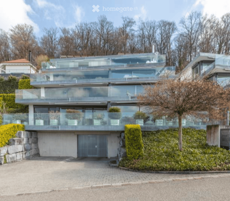 Modern two-story house with large glass balconies, garage, and landscaped garden.