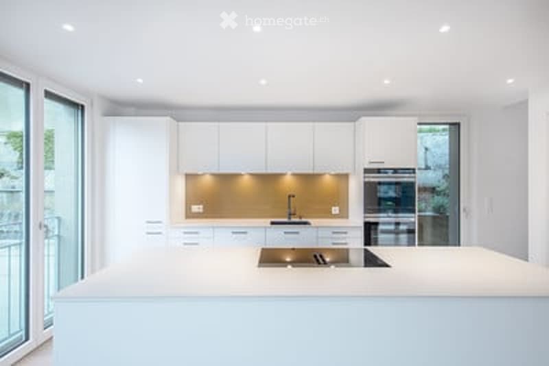 Modern, minimalist kitchen with white cabinets, a central island, and built-in appliances.