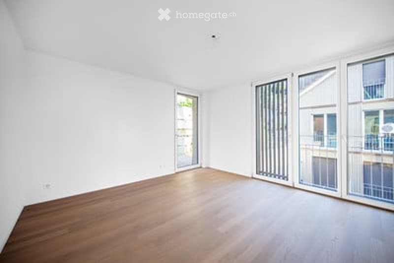 Empty room with wooden flooring, white walls, and large sliding glass doors leading to a balcony.