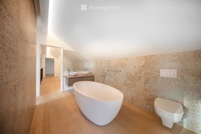 Modern bathroom with a freestanding bathtub, toilet, sink, and vanity. Light wood flooring and textured stone walls.