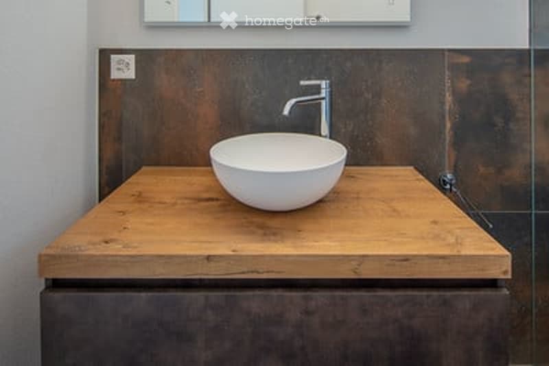Modern bathroom with a wooden countertop, white sink, and sleek faucet. Mirror above the sink.